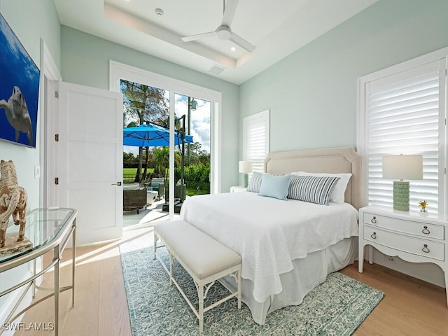 bedroom featuring a tray ceiling, access to exterior, light hardwood / wood-style floors, and ceiling fan