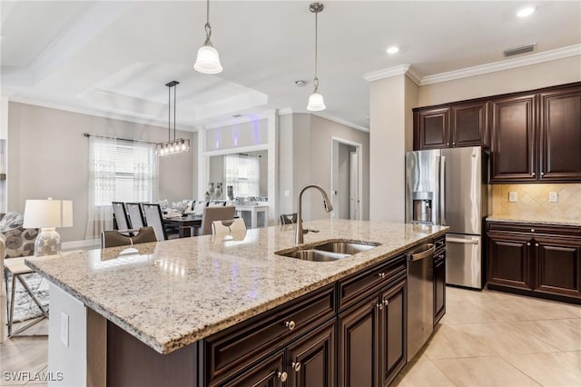 kitchen featuring dark brown cabinetry, sink, stainless steel appliances, decorative light fixtures, and a center island with sink