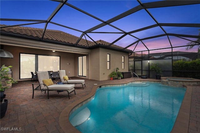 pool at dusk with glass enclosure, an in ground hot tub, and a patio