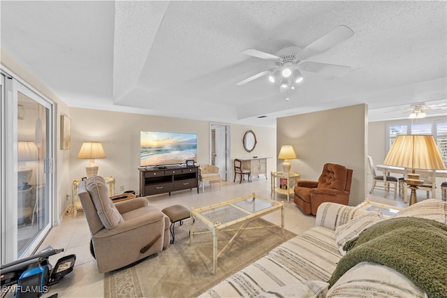 living room featuring a textured ceiling, light tile patterned floors, a raised ceiling, and ceiling fan