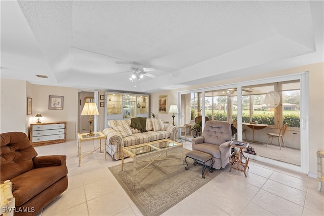 living room with a textured ceiling, a tray ceiling, light tile patterned floors, and ceiling fan