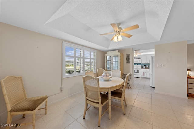 dining space with a textured ceiling, light tile patterned flooring, a tray ceiling, and ceiling fan