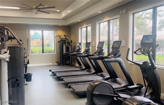 gym with ceiling fan, a healthy amount of sunlight, and brick wall