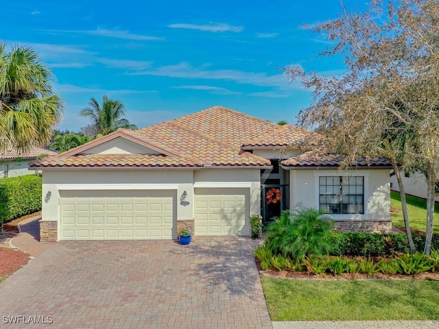 mediterranean / spanish-style house with a garage, stone siding, decorative driveway, and stucco siding