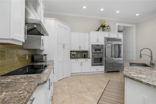 kitchen with wall chimney range hood, sink, light stone countertops, white cabinets, and appliances with stainless steel finishes