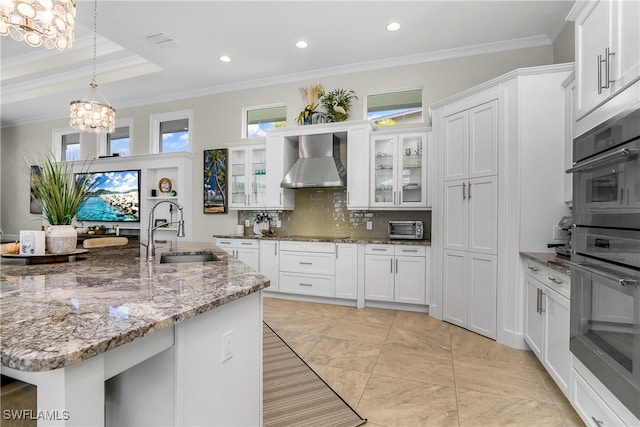 kitchen featuring sink, wall chimney exhaust hood, decorative light fixtures, white cabinets, and decorative backsplash