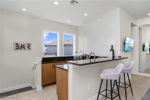 kitchen with a breakfast bar area, sink, kitchen peninsula, and dark stone countertops