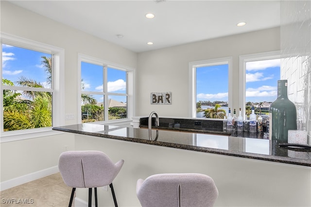 kitchen with a breakfast bar, dark stone countertops, and a healthy amount of sunlight