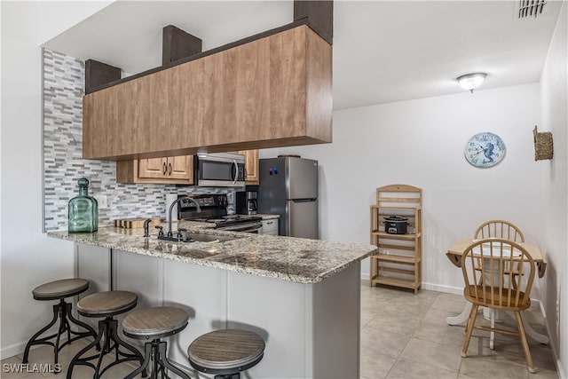 kitchen featuring kitchen peninsula, appliances with stainless steel finishes, backsplash, and stone countertops