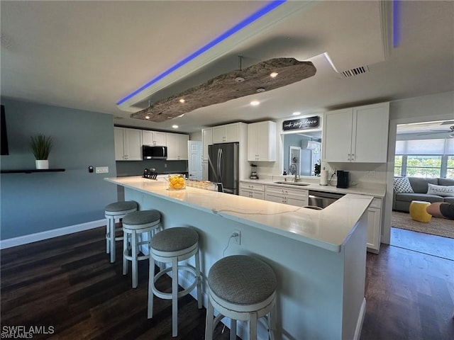 kitchen with dark hardwood / wood-style floors, a kitchen breakfast bar, stainless steel appliances, sink, and white cabinetry