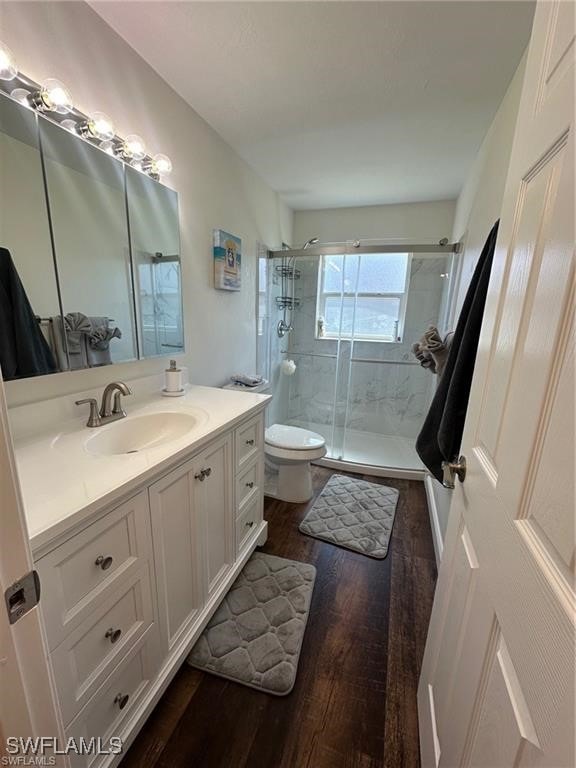 bathroom with a shower with door, vanity, hardwood / wood-style floors, and toilet