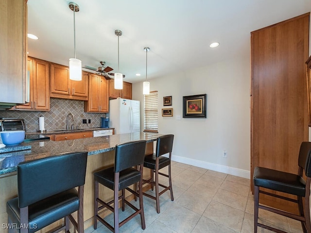 kitchen featuring pendant lighting, sink, white appliances, a kitchen breakfast bar, and dark stone countertops