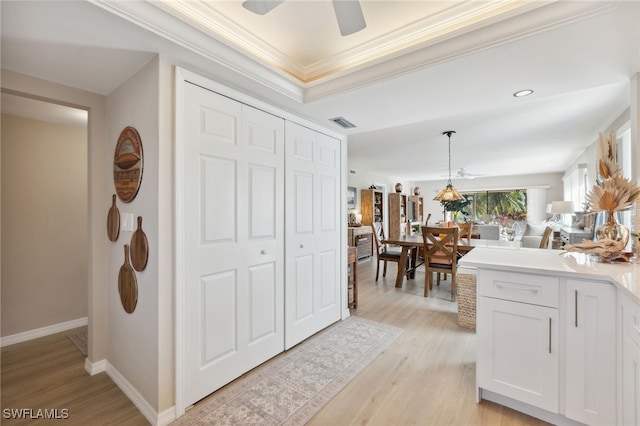 interior space with white cabinets, hanging light fixtures, ceiling fan, light hardwood / wood-style flooring, and crown molding