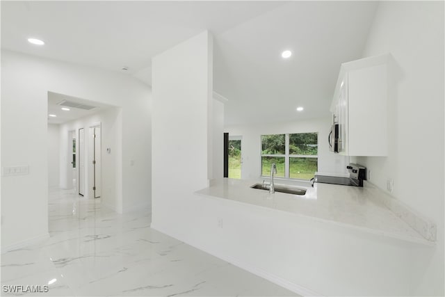 kitchen featuring kitchen peninsula, sink, black range, white cabinets, and light stone counters