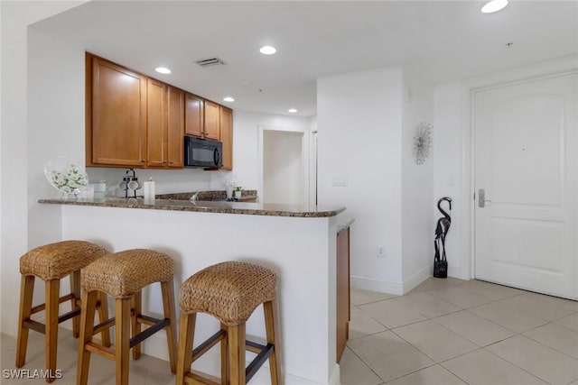 kitchen with kitchen peninsula, a breakfast bar area, light tile patterned floors, and dark stone countertops