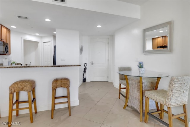 kitchen featuring light tile patterned floors, stainless steel fridge, stone counters, and a breakfast bar area