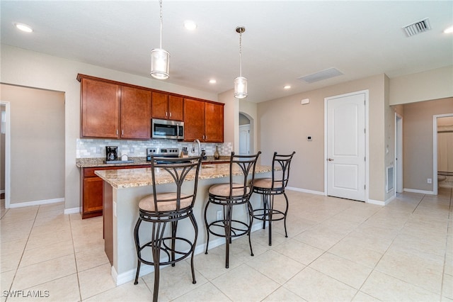 kitchen featuring light stone countertops, tasteful backsplash, hanging light fixtures, appliances with stainless steel finishes, and a center island with sink