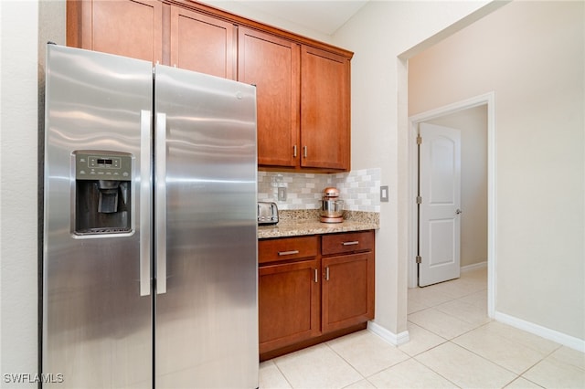 kitchen featuring stainless steel refrigerator with ice dispenser, light stone countertops, backsplash, and light tile patterned floors