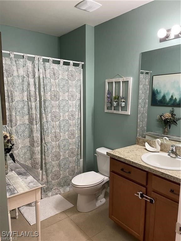 bathroom with walk in shower, vanity, tile patterned flooring, and toilet