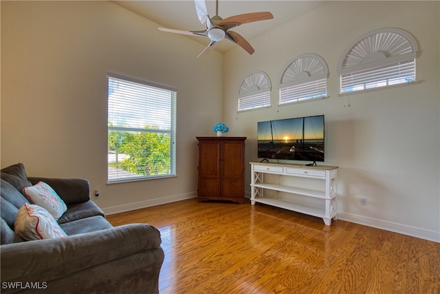 living room with hardwood / wood-style flooring, ceiling fan, and a towering ceiling