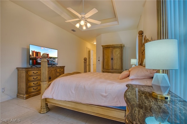 tiled bedroom with ceiling fan and a tray ceiling