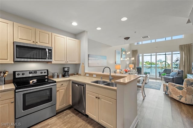 kitchen with kitchen peninsula, stainless steel appliances, sink, decorative light fixtures, and light wood-type flooring