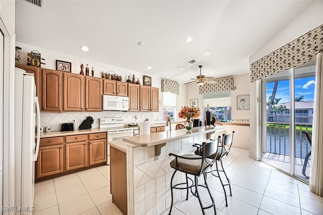 kitchen featuring tasteful backsplash, a breakfast bar, light countertops, light tile patterned floors, and white appliances