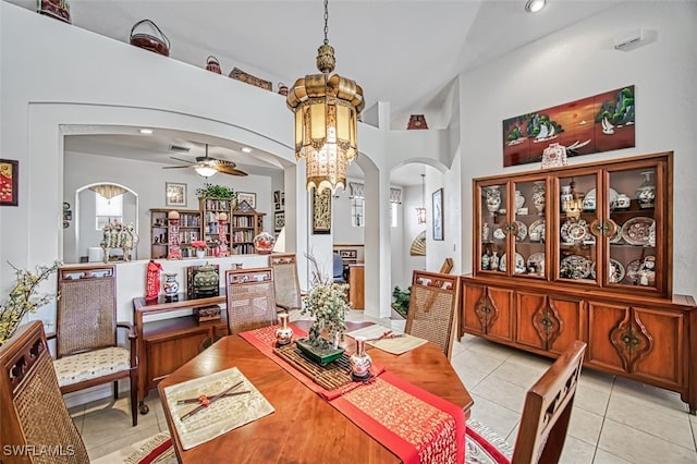 tiled dining space with a towering ceiling and ceiling fan with notable chandelier