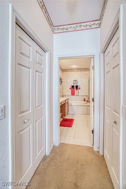 corridor featuring a textured ceiling, light tile patterned flooring, and light carpet