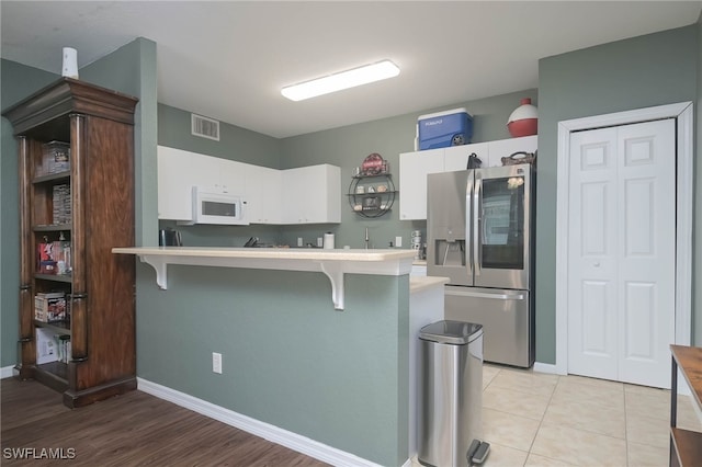 kitchen with a breakfast bar, white cabinetry, stainless steel refrigerator with ice dispenser, and kitchen peninsula