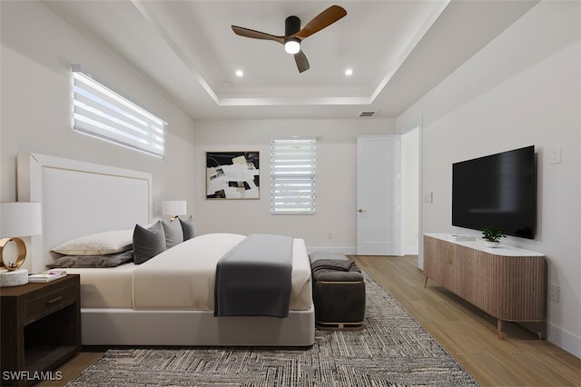 bedroom featuring hardwood / wood-style flooring, ceiling fan, a tray ceiling, and multiple windows