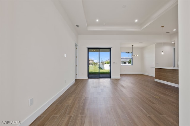 unfurnished living room with wood-type flooring, an inviting chandelier, and a raised ceiling