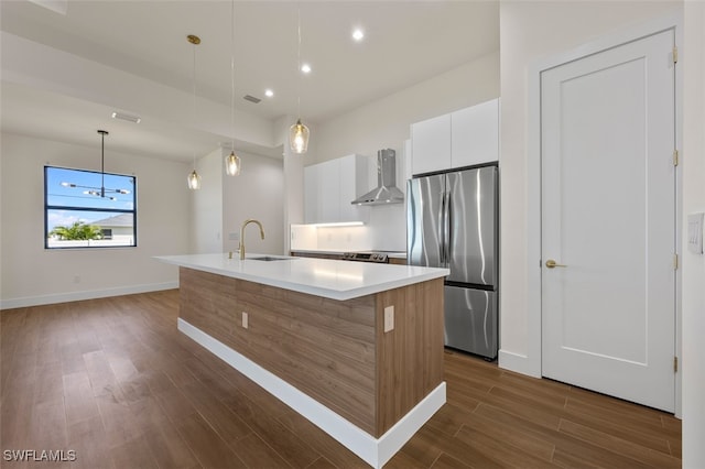 kitchen with a center island with sink, white cabinets, sink, wall chimney exhaust hood, and stainless steel refrigerator