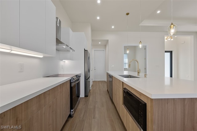 kitchen with stainless steel appliances, sink, wall chimney range hood, white cabinetry, and hanging light fixtures