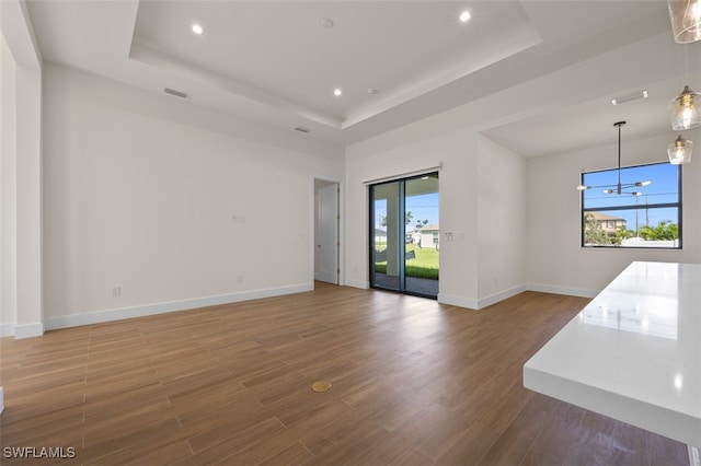 unfurnished living room featuring a tray ceiling, hardwood / wood-style flooring, and a notable chandelier