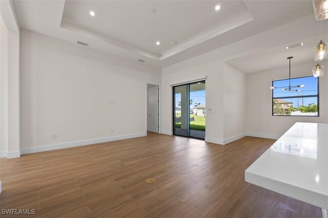 209 Kismet Pkwy E, Cape Coral, FL 33909 - unfurnished living room with visible vents, baseboards, wood finished floors, and a tray ceiling