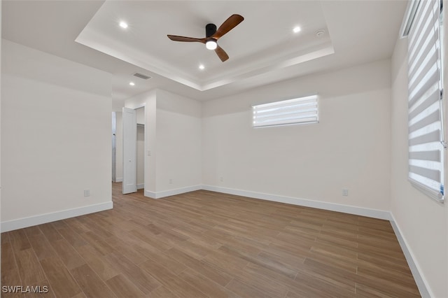 empty room featuring a tray ceiling, ceiling fan, and wood-type flooring