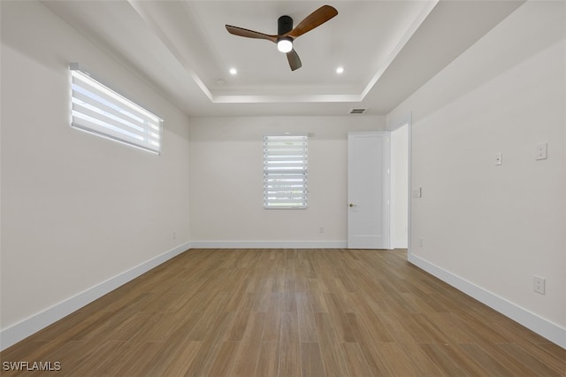 unfurnished room featuring a raised ceiling, ceiling fan, and light hardwood / wood-style flooring