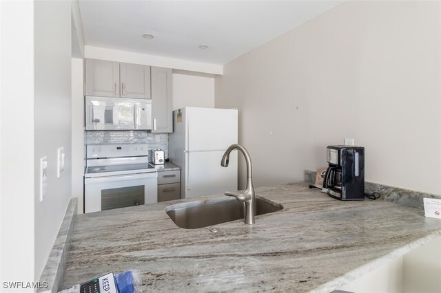 kitchen featuring white appliances, sink, gray cabinets, light stone counters, and decorative backsplash