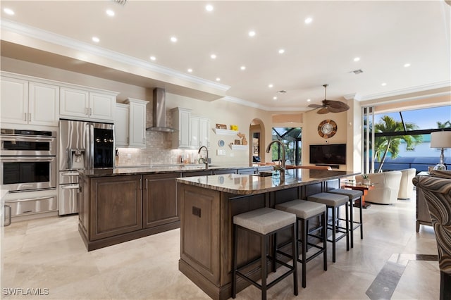 kitchen featuring wall chimney range hood, stainless steel appliances, dark stone counters, and a large island