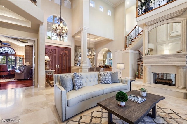 living room featuring ornate columns, ornamental molding, ceiling fan with notable chandelier, and a high ceiling