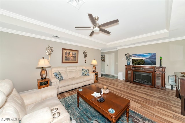 living room featuring crown molding, ceiling fan, a raised ceiling, and light wood-type flooring