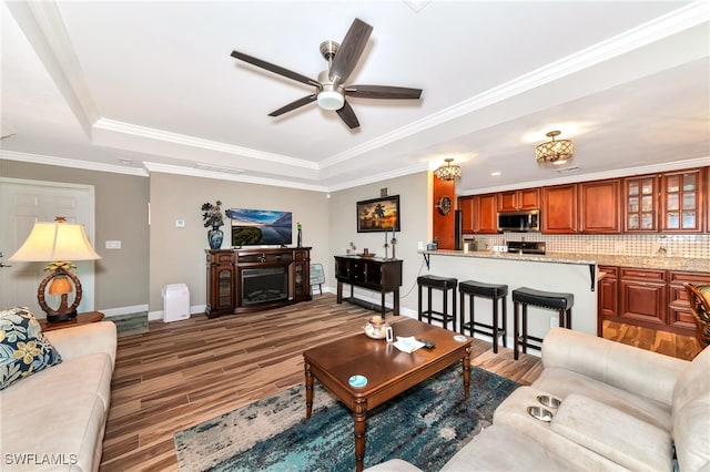 living room with ornamental molding, wood-type flooring, a tray ceiling, and ceiling fan