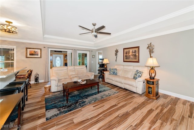 living room with light hardwood / wood-style floors, ornamental molding, and a tray ceiling