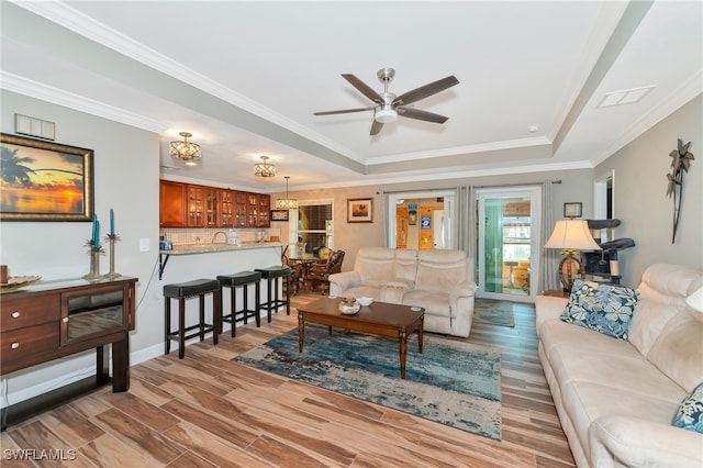 living room with light hardwood / wood-style flooring, sink, crown molding, a raised ceiling, and ceiling fan