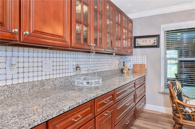 kitchen with crown molding, decorative backsplash, light stone counters, and light wood-type flooring