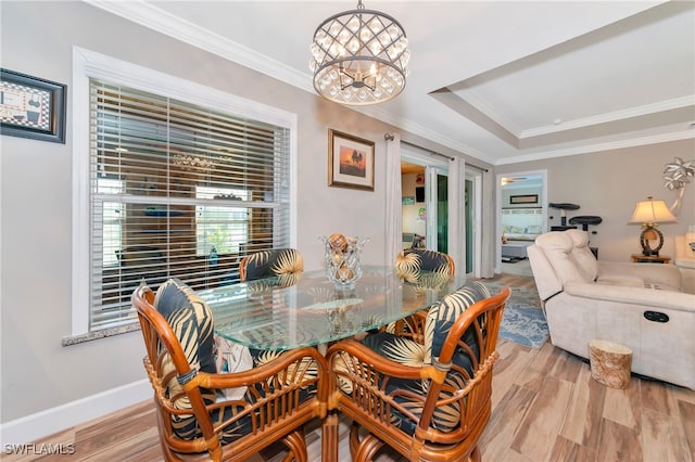 dining area with crown molding, a notable chandelier, light wood-type flooring, and a raised ceiling