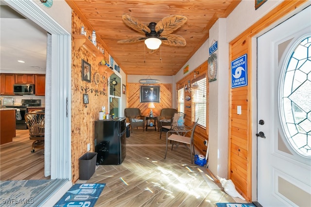 foyer featuring ceiling fan, wooden ceiling, light wood-type flooring, vaulted ceiling, and wood walls