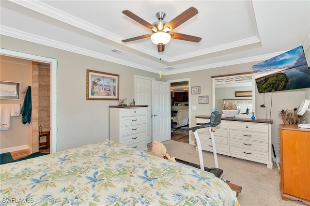 carpeted bedroom with ensuite bath, ornamental molding, a tray ceiling, and ceiling fan