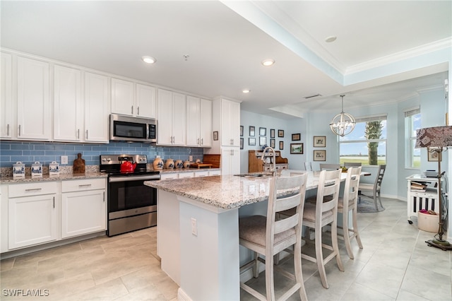 kitchen featuring ornamental molding, appliances with stainless steel finishes, white cabinets, and an island with sink